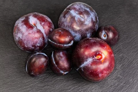 Plums different varieties and sizes on black flat slate plate Stock Photos