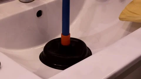 A plunger being used inside a white bathroom sink to unclog blocked pipes s.. Stock Footage 321833717