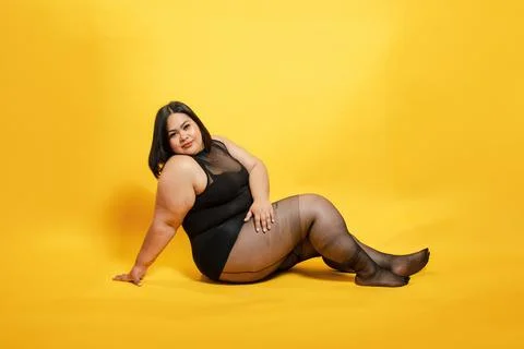 Plus size asian model posing on yellow background, embracing body positivit.. Photos