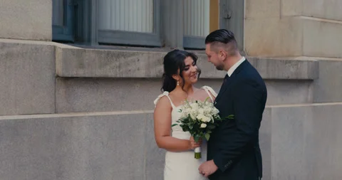 Plus-size bride and groom stand happily facing each other on a city street, she Vidéo 347011586