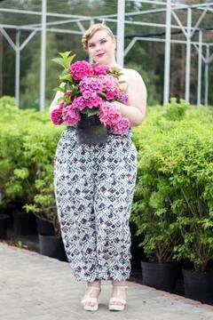 Plus size Girl keeps pot with blooming plant  in greenhouse Stock Photos