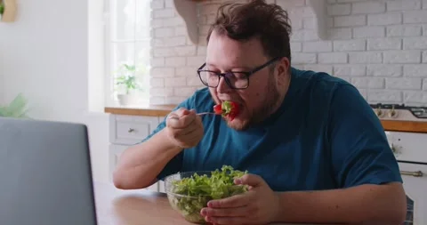 Plus size man eating salad to lose weight, person with obesity sitting with Video stock 334101810
