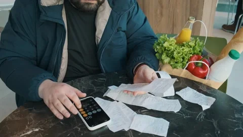 Plus size man reviewing receipts and calculating grocery expenses using Stock Footage 285537566