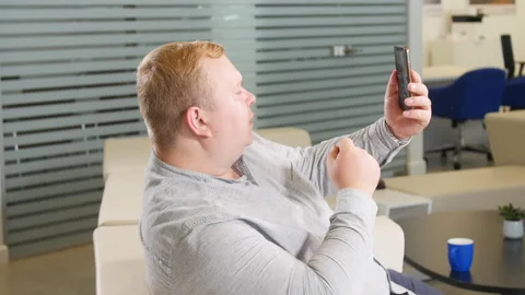 Plus size man talks on a video call phone in office Stock Footage 232609774