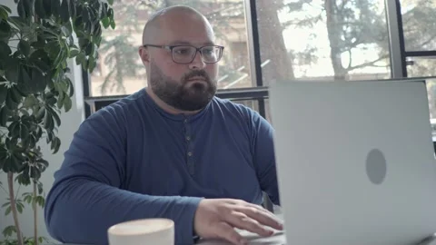 Plus size men in glasses working at laptop in cafe Stock Footage 231073788