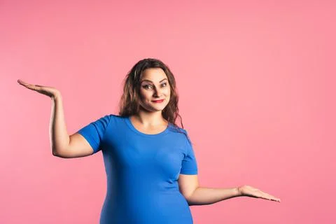 Plus size model in a blue T-shirt gestures on pink background Photos