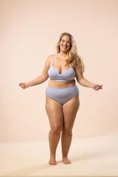 Plus size model in blue underwear smiles on beige background, copy space Stock Photos