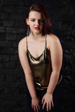 Plus size model in a gold blouse and black jeans on a brick loft background. Stock Photos