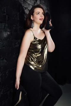 Plus size model in a gold blouse and black jeans on a brick loft background. Stock Photos
