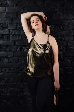 Plus size model in a gold blouse and black jeans on a brick loft background. Stock Photos