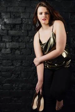 Plus size model in a gold blouse and black jeans on a brick loft background. Stock Photos