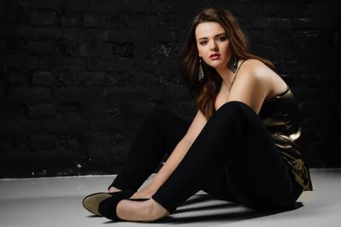 Plus size model in a gold blouse and black jeans on a brick loft background. Stock Photos