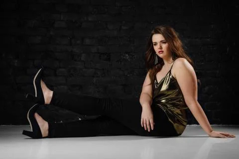Plus size model in a gold blouse and black jeans on a brick loft background. Foto stock