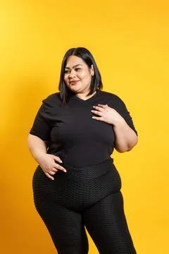 Plus size model posing with hand on chest, embracing body positivity on yel.. Photos