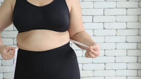 Plus size or big size girl use measuring tape to measure her waist in the room Stock Footage 120716937