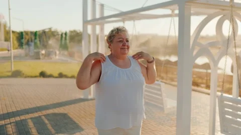Plus size pensioner rotating shoulders doing physical therapy outside. fitness Stock Footage 340992352