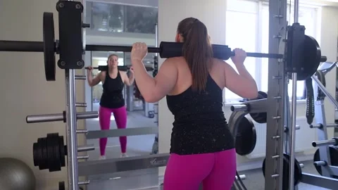 Plus size woman doing exercises on Smith Machine. Squats on a simulator with a b Stock Footage 313258634