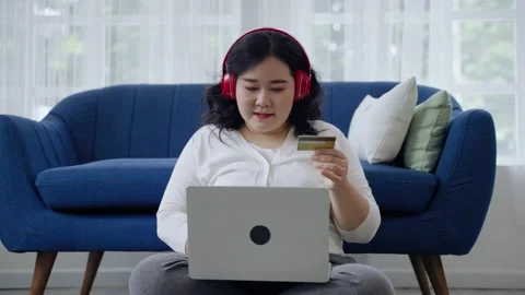 Plus-size woman is happily using her online shopping credit card in her room. Stock Footage 159732573