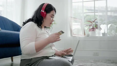 Plus-size woman is happily using her online shopping credit card in her room. Stock Footage 164468416