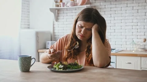 Plus size woman sitting at table, feeling unhappy with diet not wanting to eat Stock Footage 143567724