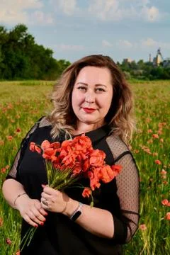 Plus sized woman in a black dress on a field of green wheat and wild poppies. Stock Photos