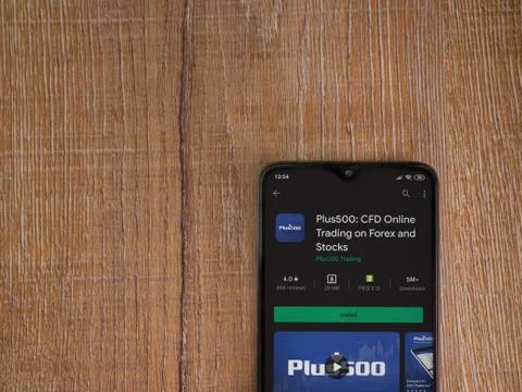 Plus500 app play store page on the display of a black mobile smartphone on wo Stock Photos