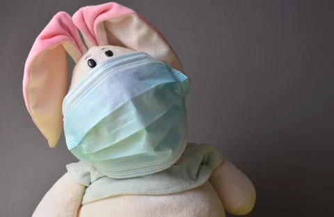 Plush hare in a mask on a gray background. Stock Photos