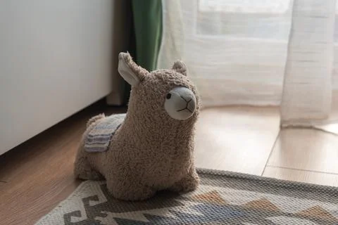 Plush llama on patterned rug by sunlit window in Malbork apartment Stock Photos