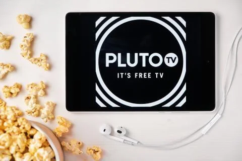 Pluto TV on the screen of the tablet with popcorn box and Apple earphones on the Stock Photos