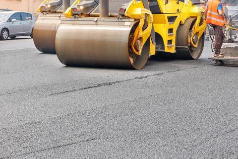Pneumatic steam road rollers compact fresh asphalt on the road in front of a  Stock Photos