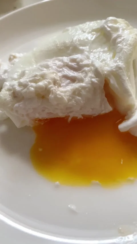 Poached egg is broken with a fork on a white plate Stock Footage 221169827