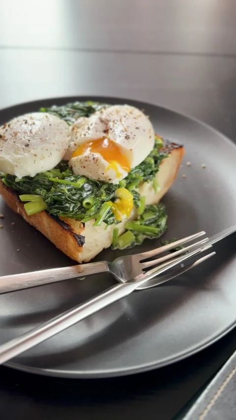 Poached egg is cut with a knife on whole grain toast with creamy spinach Stock Footage 319974702