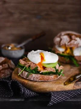 Poached egg on a full grain bun with avocado, cucumber, kiwi and arugula on a Stock Photos