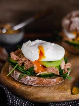 Poached egg on a full grain bun with avocado, cucumber, kiwi and arugula on a Stock Photos