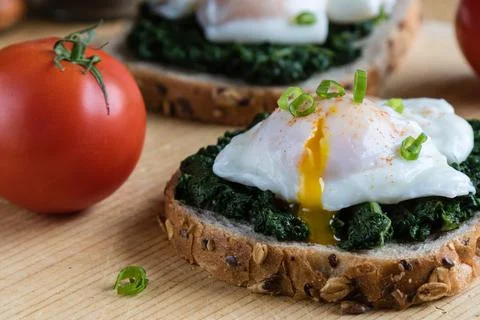 Poached egg on a piece of brown bread with spinach on a wooden table Stock Photos
