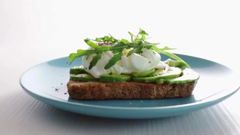 Poached egg on a slice of organic bread,hands spread arugula on toast with .. Stock Footage 251455637