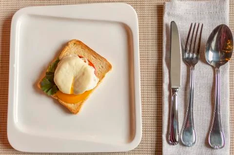 Poached egg, on a toasted slice of white bread with tomato and seasoning on a Stock Photos