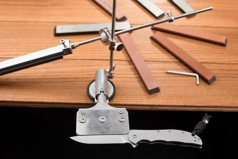 Pocket knife fixed in a manual sharpener machine and a set of whetstones Foto stock