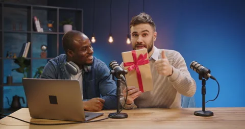 Podcast hosts promoting giveaway with present box on air, recording online show Stock Footage 328973341