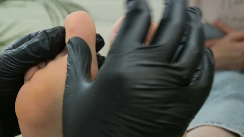 A podiatrist in black gloves compares two legs of a client. The pedicure tea Stock Footage 208064041