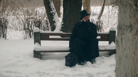 Point of interest shot: A man in a black coat sits thoughtfully on a bench in Vídeos de archivo 102166023