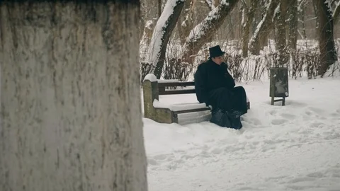 Point of interest shot: A man in a black coat sits thoughtfully on a bench in Vídeos de archivo 102171534