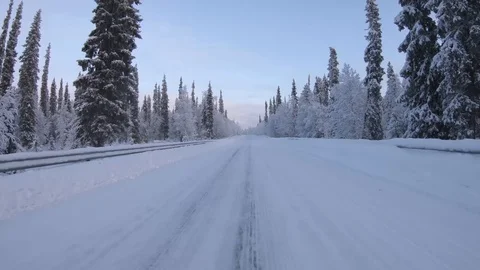 Point of view angle of driving a car on icy road through snowy forest landscape Stock Footage 120696329