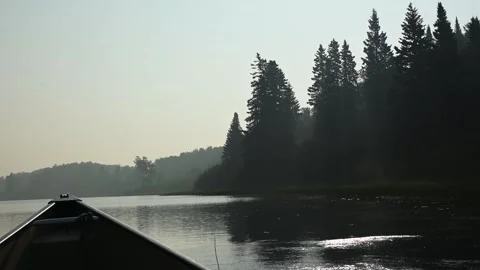 Point of view from a canoe drifting on a smoke covered northern lake with spruce Stock Footage 333074861