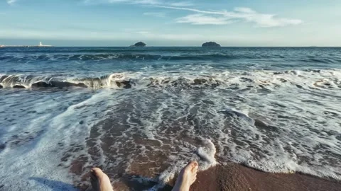 Point of View captures bare feet on ocean shore as waves roll in with distant Stock Footage 326769986