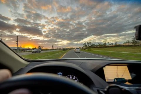 Point of view driving along palm-lined street at sunset with steady traffic f Stock Photos