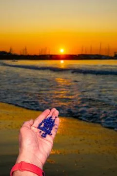 Point of view hand holding plastic pellets near the seaside. Ecological disaster Stock Photos
