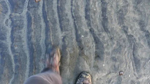 Point of view of hiking boots walking through shallow water on a sandy beach. Stock Footage 129658624