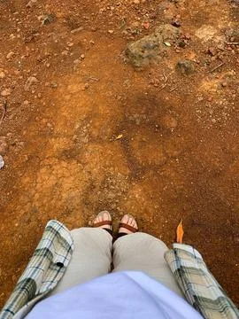 Point of view looking down at feet standing on dusty red earth during an ou.. Stock Photos