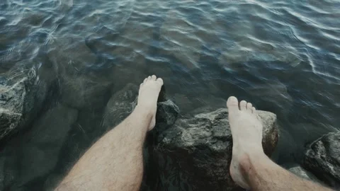 Point of view of a mans feet on rocks on the shore of a river Stock Footage 301103637